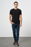Man wearing a black t-shirt and blue jeans standing against a plain white background