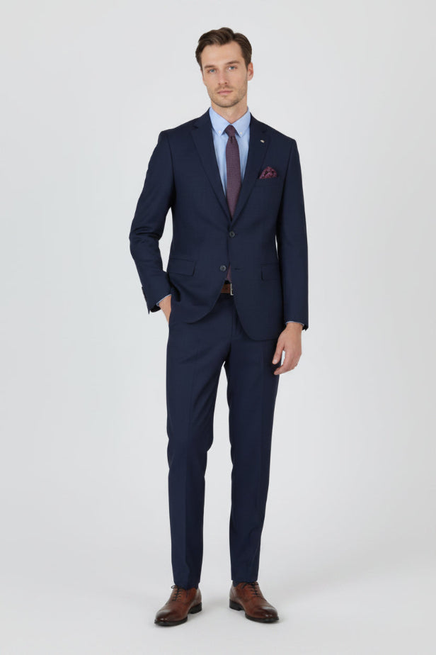 Man wearing a navy suit with a white shirt and brown shoes on a light gray background